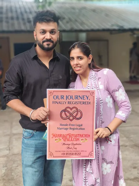 Couple outdoors holding an Our Journey, Finally Registered placard