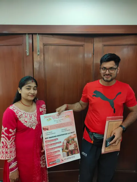 Couple holding a marriage-registration leaflet and documents indoors